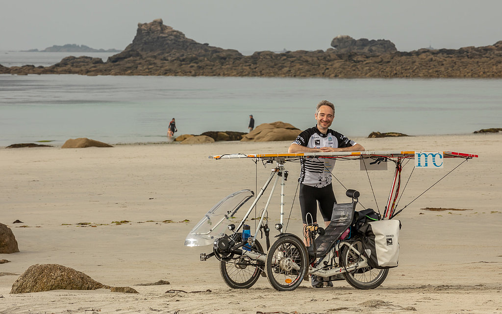 Adrien Acres sitting in his recumbent solar bike on a beach