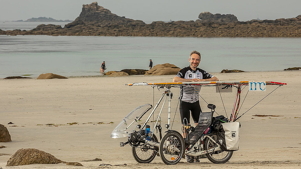 Adrien Acres sitting in his recumbent solar bike on a beach